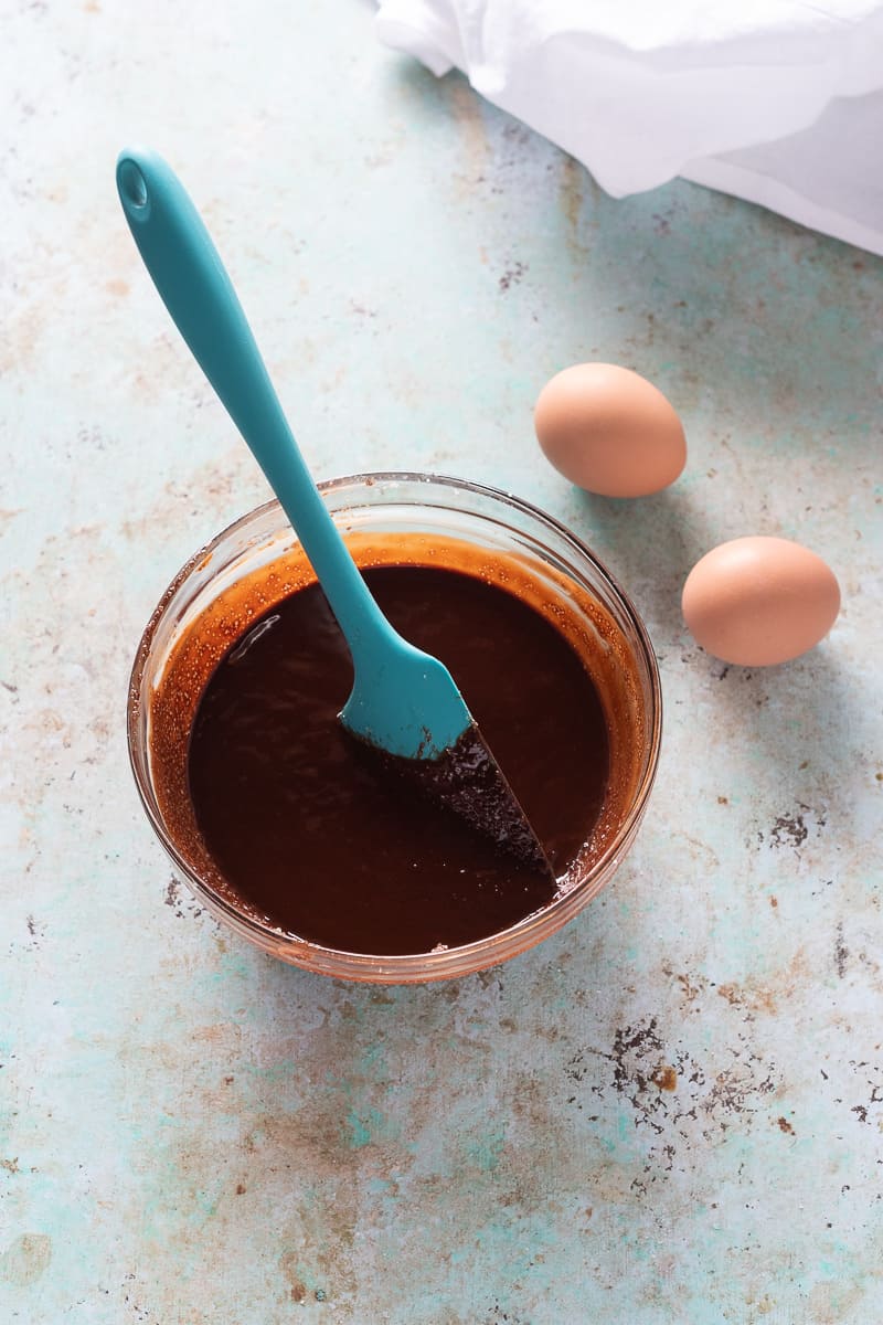 一碗融化的巧克力，黄油和糖，旁边放着两个鸡蛋