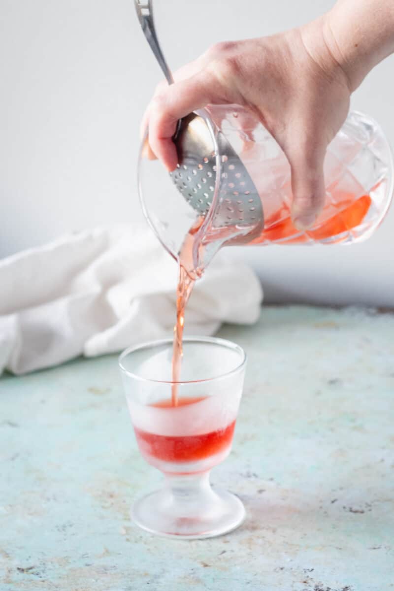 用Julep过滤网将一杯内格罗尼酒过滤到冰过的玻璃杯中